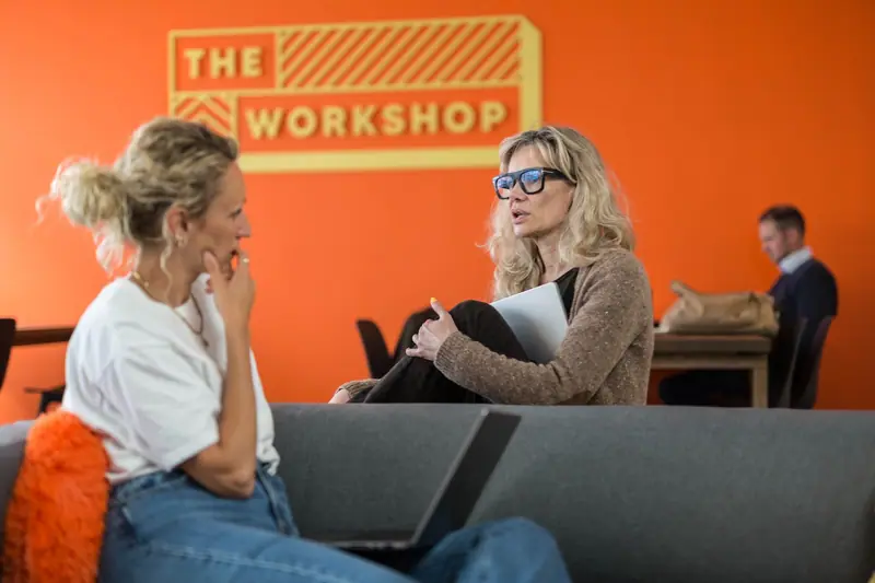 Two members talking on the Workbench sofa in front of the orange Workshop wall
