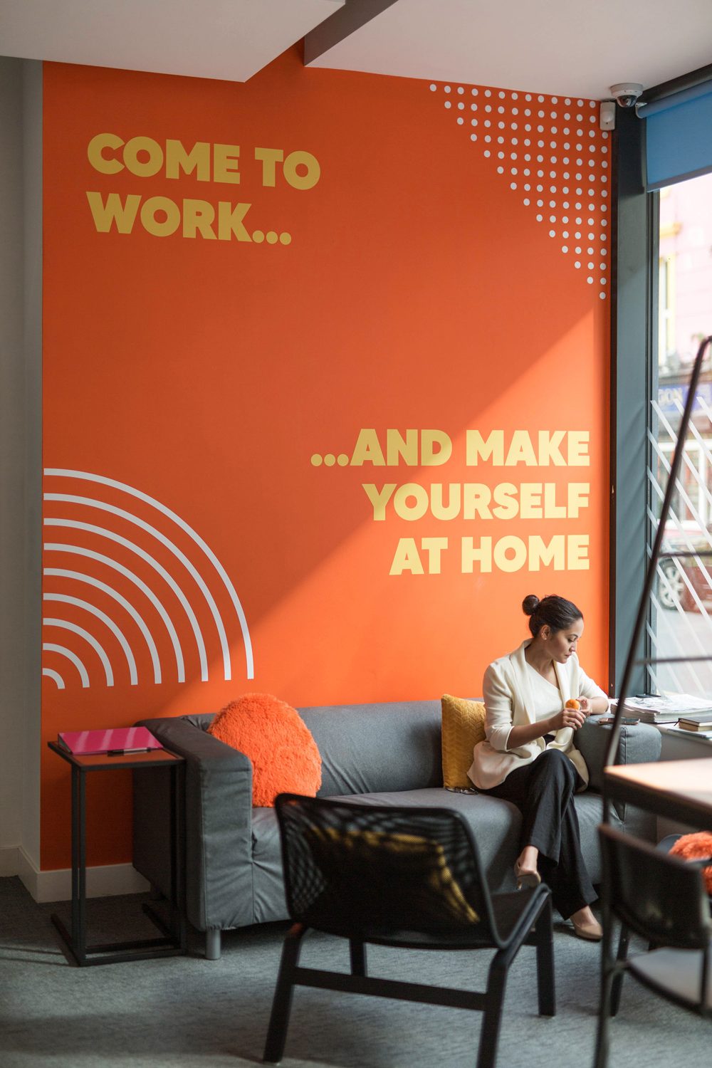 A member on the sofa under the orange 'Come to work... and make yourself at home' wall